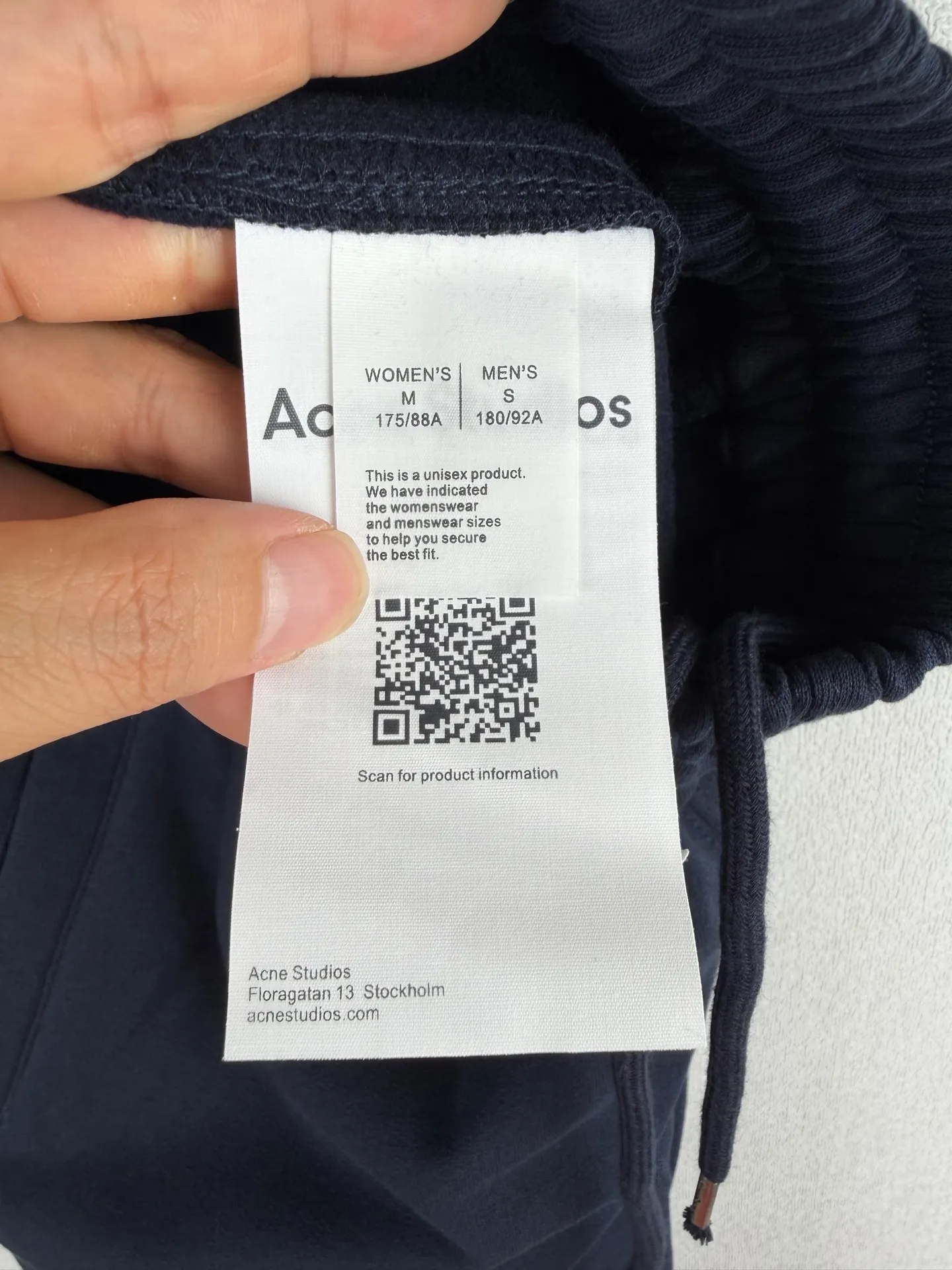 ACNE STUDIOS embroidered logo fleece sweatpants wide-leg trousers. Fabric: 32-count double yarn top + 16-count terry bottom yarn G The veil is made of 32-count fine yarn. The high-count yarn is smooth and delicate. After weaving, it forms a smooth and compact surface. It not only resists pilling and wear-resistant, but also gives the fabric a touch as delicate as skin. The base yarn is made of 16-count roving. The low-count yarn is fluffy and hairy. It naturally forms a rich terry layer during the weaving process, providing a sufficient source of fiber for subsequent sanding. This combination of fine surfaces and thick soles strikes a perfect balance between warmth and skin-friendliness. Mechanical sanding is the soul process of this fabric. By rubbing the bottom surface of the roller wrapped with emery leather at high speed, the fiber ends of the 16-count roving are evenly pulled out and cut off, forming a dense and uniform short pile layer. The smoothness and neatness of needle embroidery and the soft velvet feel of brushed fabrics form a material dialogue between hardness and softness. The embroidery area is smooth and crisp, with sharp lines, like delicate inscriptions carved on a rich suede canvas; while the surrounding brushed fabric presents a soft matte natural texture. The spacing between stitches is consistent and the strength is balanced to ensure that each stitch is placed accurately. This rigorous stitching structure makes the edges of the logo present a sharp and clear outline, and the strokes of the text are full and smooth. Even the curved turning points of the floral fonts can achieve a smooth transition through the connection of tight stitches.